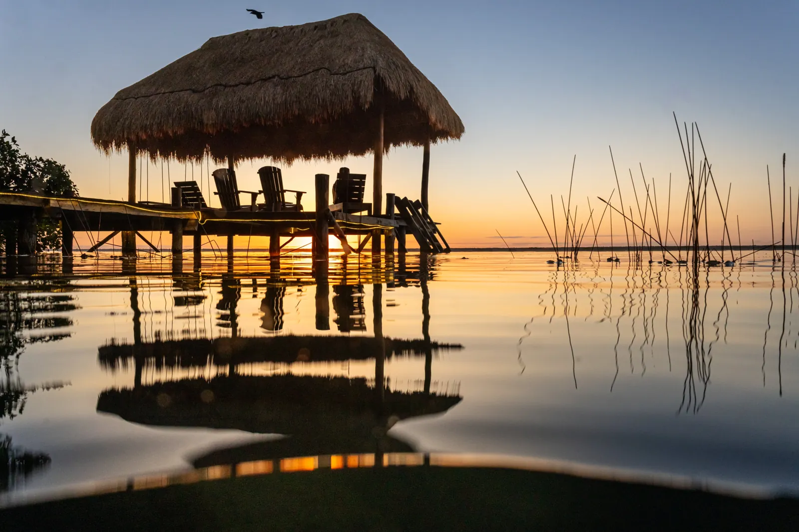 Amanecer sobre la laguna de Bacalar, con el muelle y la palapa de Villa Alegre reflejados en el agua quieta